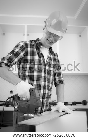 worker with jigsaw shortens floorboard, black and white image