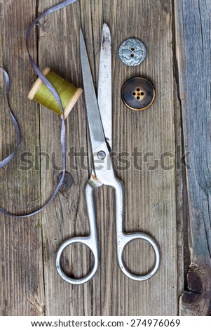 vintage dressmaker scissors, bobbin with thread and buttons on the boards of the old aged table