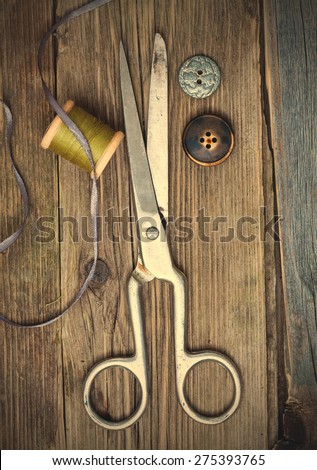 vintage dressmaker scissors, bobbin with thread and buttons on the boards of the old aged table. instagram image retro style