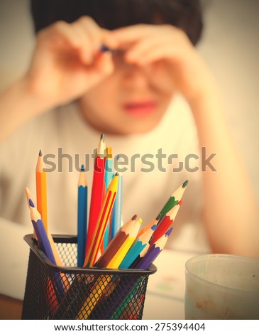 colored pencils to draw in a holder and a child on the background. focus on pencils. instagram image retro style