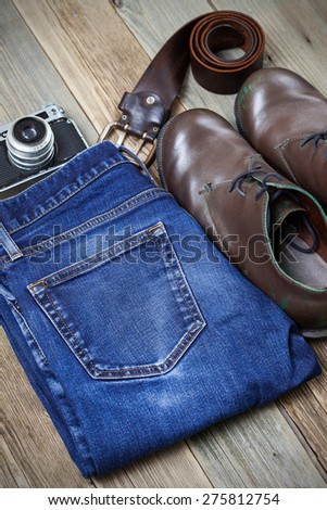 Still life with brown boots, blue jeans, leather belt and rangefinder camera on aged textured boards