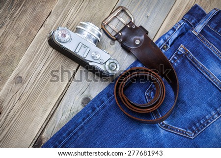 rangefinder camera, vintage leather belt and blue jeans on the old wooden boards. Kit for the traveler