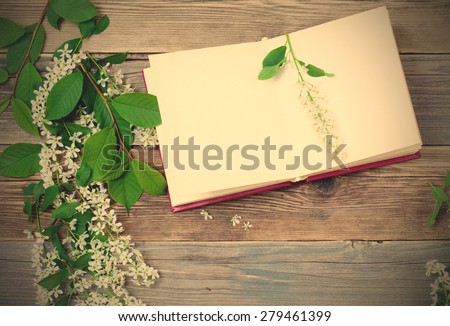 Blossoming bird-cherry and vintage open book on the aged  boards of the ancient table. Still life. instagram image filter retro style