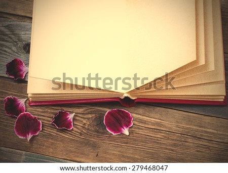 open book with petals of geraniums on the page. Still on the old wooden textured boards. instagram image filter retro style