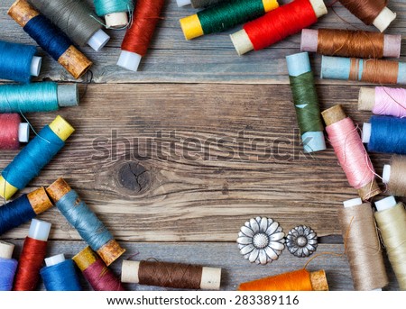 vintage reels of varicolored thread and old flower buttons on the textured surface of the ancient tailor\'s table