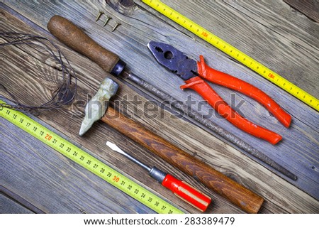 ancient cylindrical rasp, screws, old screwdriver, pliers, wire, hammer and yellow measuring tape on aged textured boards