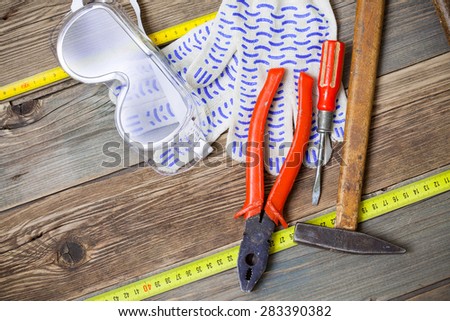 vintage hammer, old pliers, screwdriver, tape measure, gloves and safety glasses on aged  textured boards bench. still life with working tools