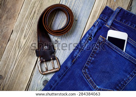 old blue jeans, vintage leather belt and smartphone on aged boards. still life in a nostalgic manner
