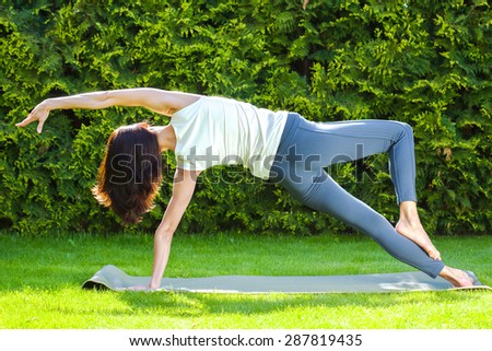 beautiful adult woman doing yoga on green grass in park