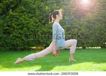 pretty adult woman doing yoga on green grass in summer park