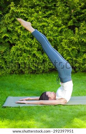 pretty woman doing yoga on green grass in park at summer morning
