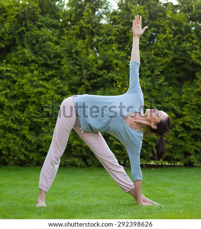 pretty adult woman doing yoga on green grass in summer park