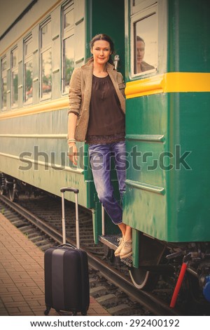 Travel portrait of a beautiful adult woman with luggage on the steps of the passenger car. instagram image filter retro style