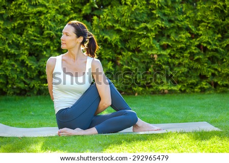pretty woman doing yoga on green grass in park at summer day