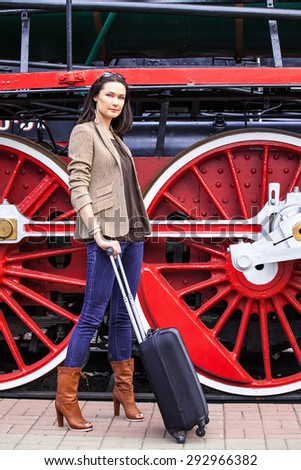 retro journey for a beautiful lady. pretty adult woman with luggage near the huge wheels of an old steam locomotive to travel