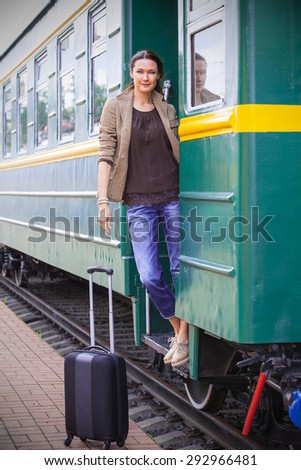 Travel portrait of a beautiful adult woman with luggage on the steps of the passenger car