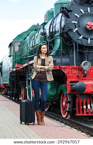retro journey for a beautiful woman. pretty adult woman with luggage near the old steam locomotive for travel