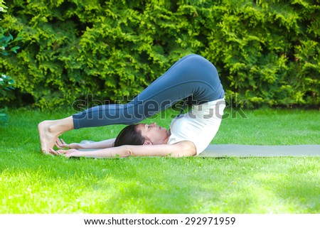 beautiful adult woman doing yoga on green grass in park at summer day