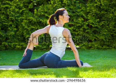 beautiful adult woman doing yoga on green grass at summer day in park at summer morning