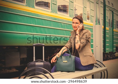 beautiful woman talking on a cell and wait for the train to go on a retro travel by railway. instagram image filter retro style