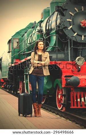 retro journey for a beautiful woman. pretty adult woman with luggage near the old steam locomotive for travel. instagram image filter retro style