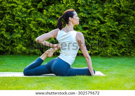 beautiful adult woman doing yoga on green grass in park at summer morning