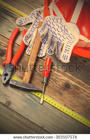 set of old tools to work, measuring tape, gloves and orange construction helmet on a vintage textured boards. instagram image filter retro style