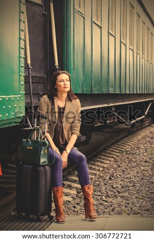 beautiful middle-aged woman traveling in a retro style. sHe is sitting on the steps of a vintage railroad car and waiting for the conductor. instagram image filter retro style
