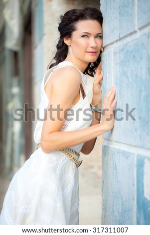 beautiful middle-aged woman in a white dress near the old stone wall