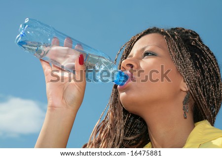 african girl in yellow gown drinking water from blue bottle on sky background