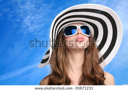 beautiful girl in striped hat and sunglasses on background blue sky