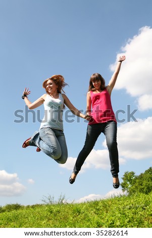 two jumping girls on green herb under blue sky in park