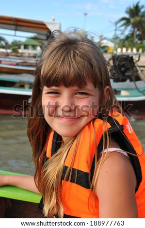 Smiling girl portrait looking at camera. She sits in boat in safety jacket.