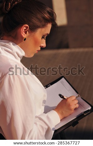 White pretty woman making note at her notepad outdoor. Rear view from out shoulder.