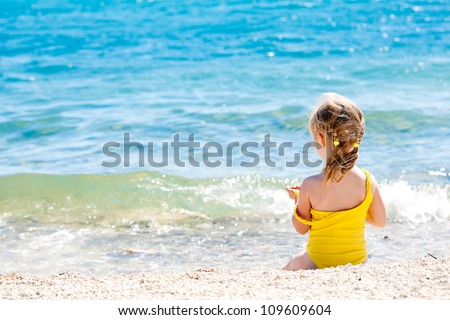 Small girl sitting back on the shore of the sea
