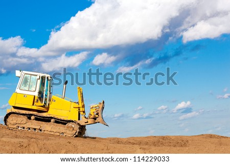 Bulldozer machine moves with raised blade on construction site during earth moving works