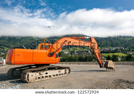Excavator with metal tracks at construction site on austrian alps background