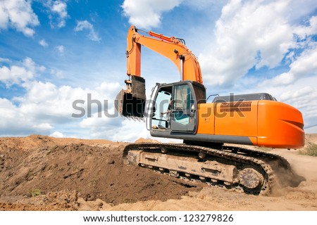Excavator machine moves with raised bucket on construction site during earth moving works