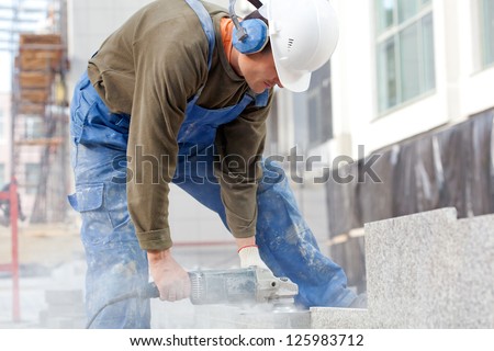 Industrial worker making horizontal cut with electric hand saw during align marble tiles at construction site