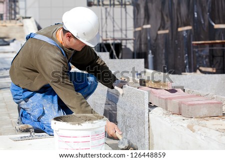 Tiler in helmet and work wear installing marble tiles at construction site Tiler in helmet and work wear installing marble tiles at construction site