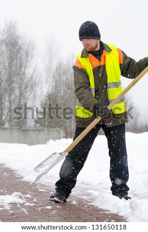 Laborer man road worker in uniform and reflective vest shoveling snow