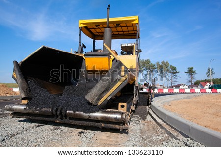 Tracked paver laying fresh asphalt pavement on top of the gravel base during road construction