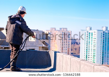 Roofer worker installing roofing felt by means of gas blowpipe torch