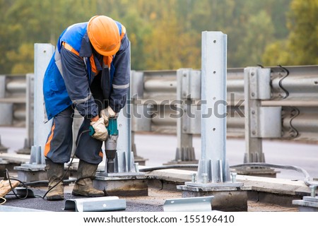 Laborer worker tightening bolts with Electric Impact Wrench tool during construction Road Works on installation traffic barrier