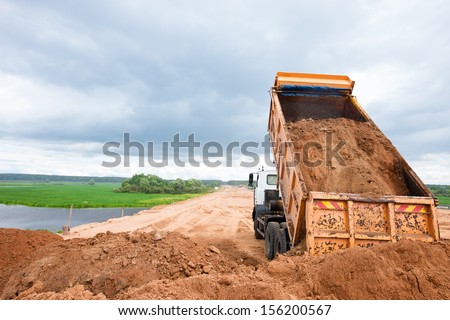 Dump truck unloading soil or sand at construction site during road works