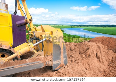 Bulldozer machine during earth moving works at construction site on nature background