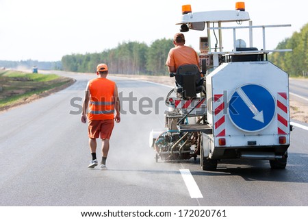 Two industrial workers with thermoplastic spray marking machine during road pavement construction works