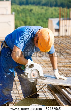 Mid adult carpenter worker cutting wood sheet with handheld saw during construction works
