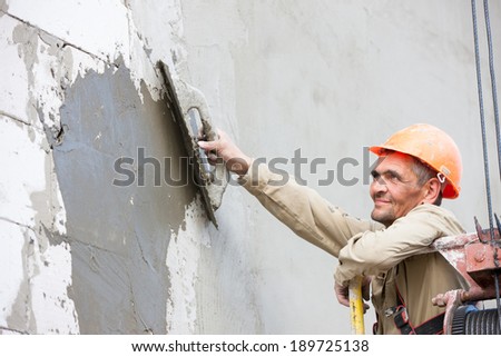 Plasterer crafts man worker plastering multi storey building wall of bricks or concrete blocks during finishing construction works