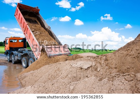 Dumper truck unloading soil or sand at construction site during road works at blue sky background